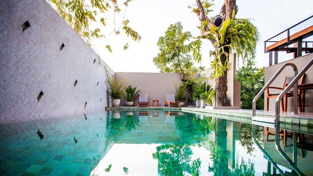 A swimming pool with clear water, surrounded by potted plants and trees. - Cinnamon Hotel Bangkok (Bangkok)