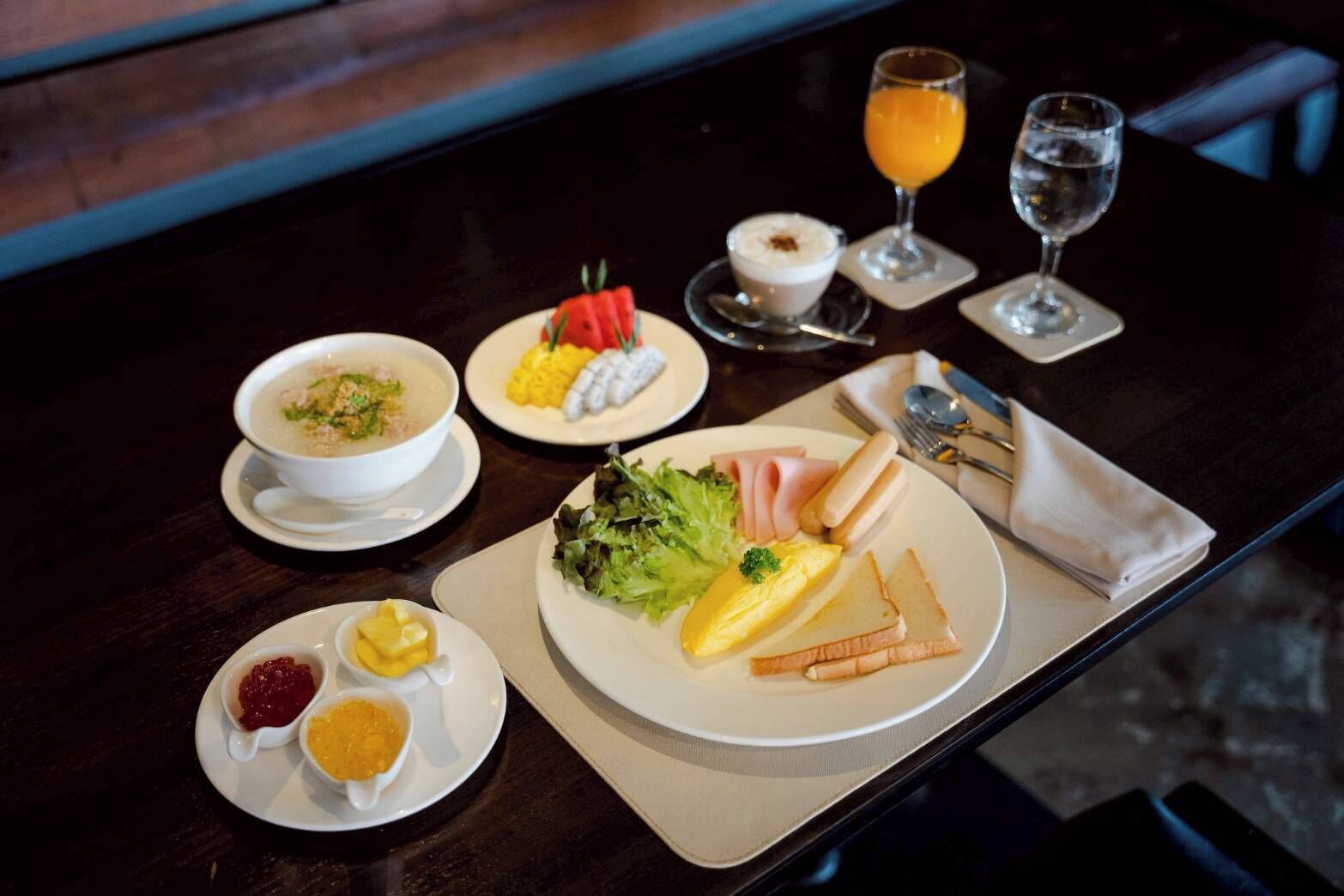 A breakfast setting with a bowl of soup, scrambled eggs, toast, and a plate of vegetables. There are also two glasses of orange juice and a cup of coffee.