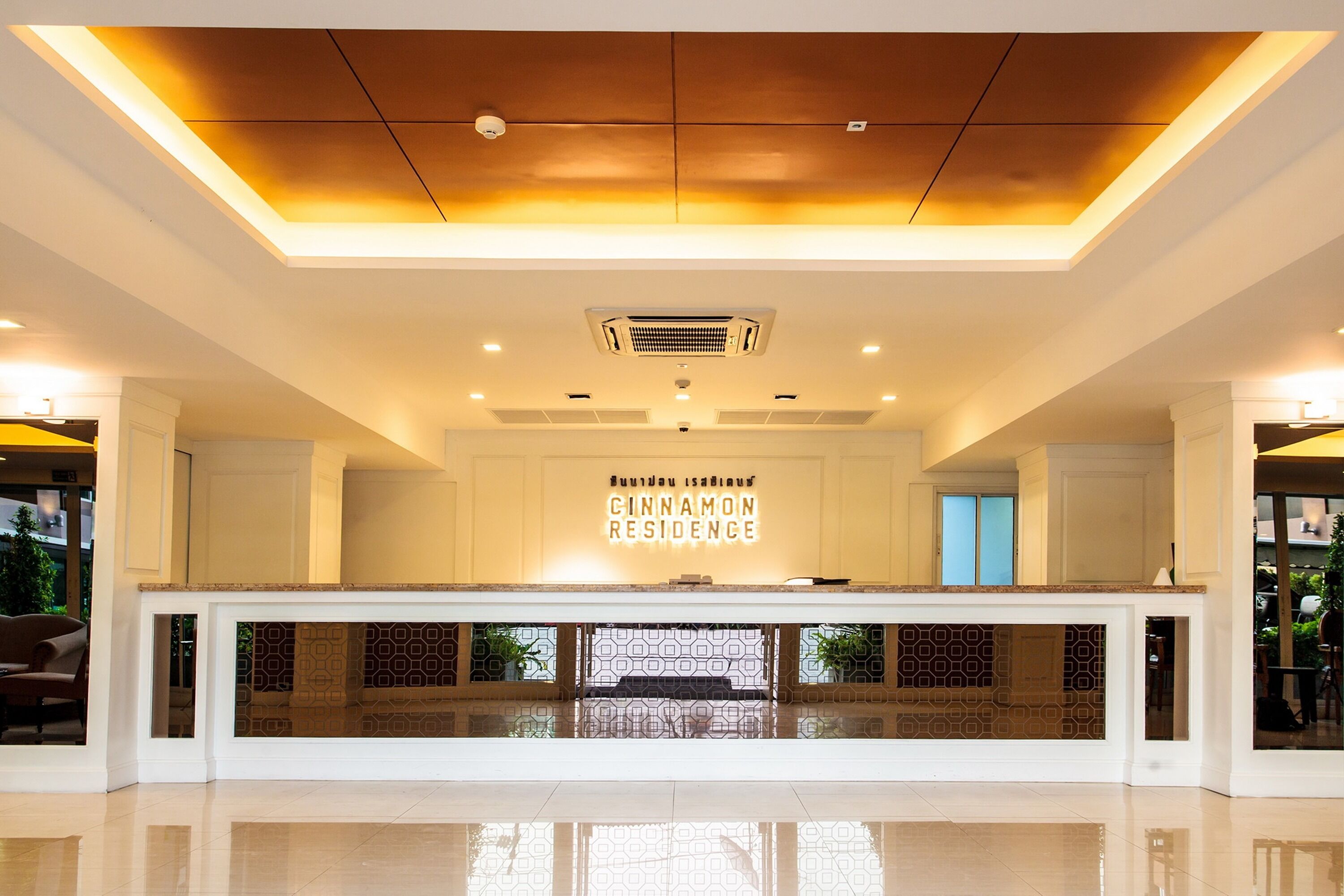 A reception area with a modern design, featuring a central counter, a ceiling with recessed lighting, and a sign that reads "Cinnamon Residence."