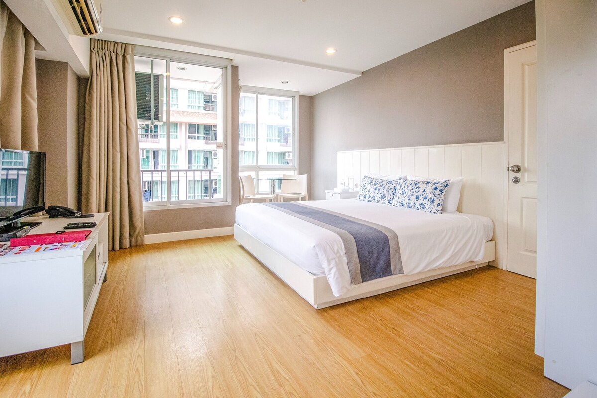 A modern hotel room with a large bed, a desk, and a window with a view of the city.