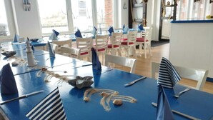 Un espace repas avec des tables bleues, des chaises blanches et des serviettes à rayures.