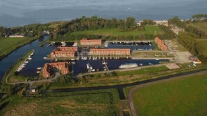 Une vue aérienne d’une marina avec de nombreux quais et des bateaux, entourée de verdure et d’un petit bâtiment.