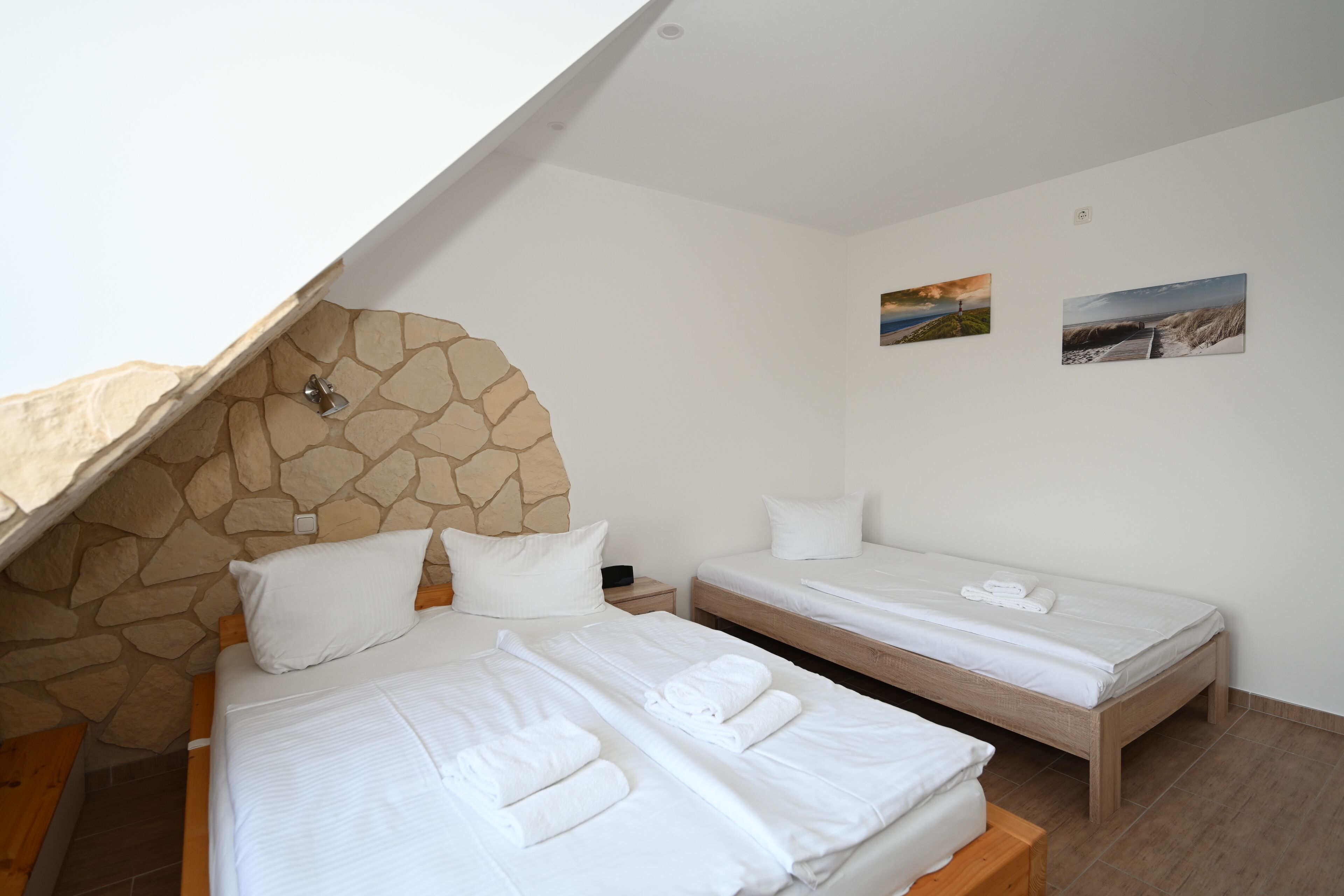 Une chambre avec deux lits, un mur en pierre et deux tableaux représentant des paysages.