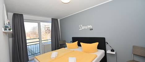 Ein modernes Schlafzimmer mit einem großen Bett, zwei Kissen, einem Nachttisch, einer Lampe und Blick ins Freie.