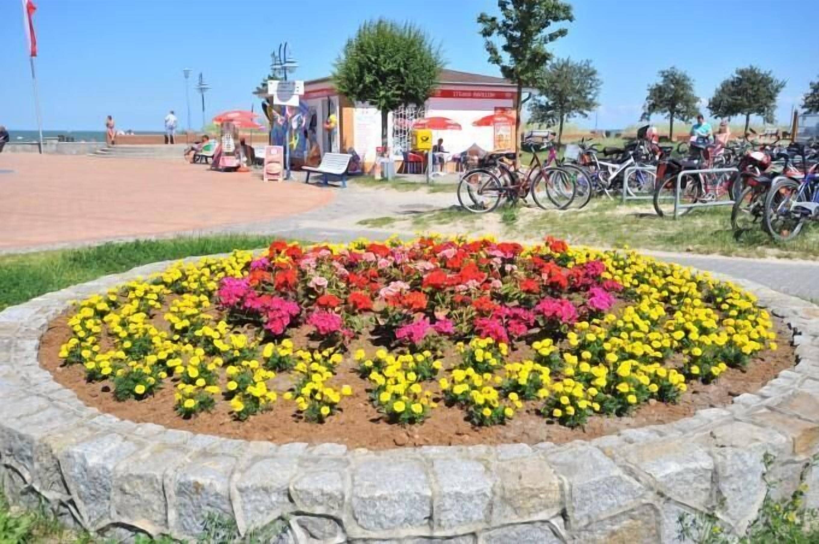 A flower bed with a stone border, a building with a red and white sign, and bicycles parked nearby.