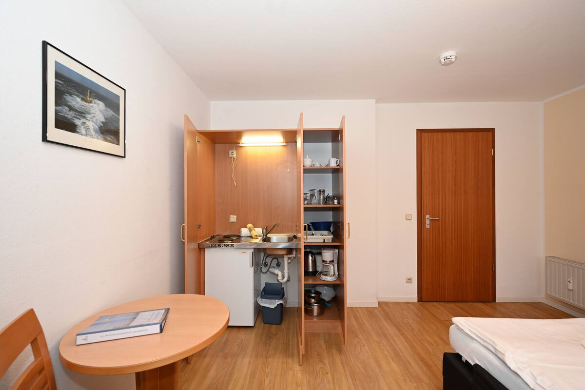 Ein kleines Zimmer mit einer Küchenzeile, einem Bett, einem kleinen Tisch und einer Tür.