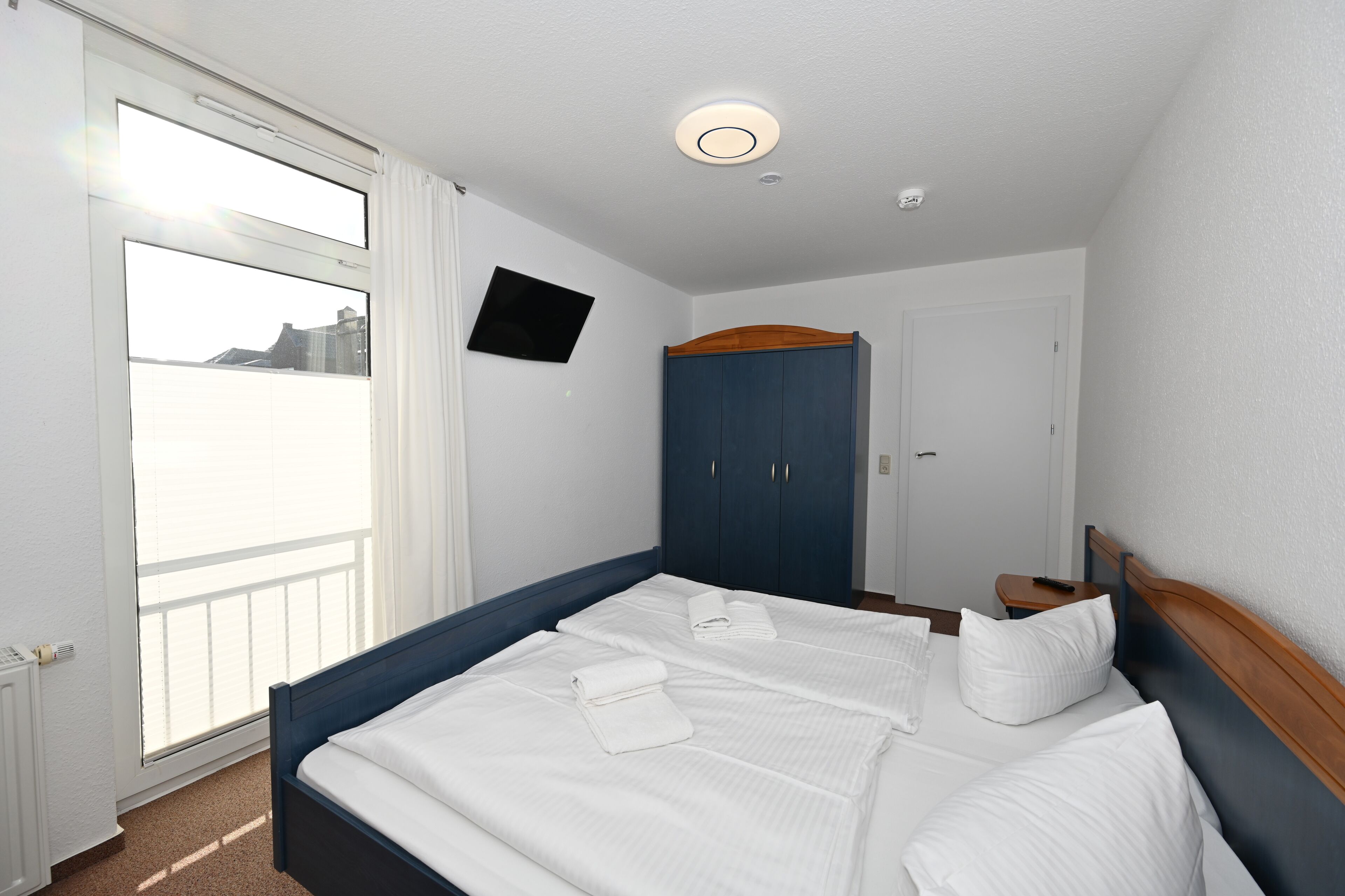A hotel room with a large bed, a wardrobe, a television on the wall, and a window with a view.