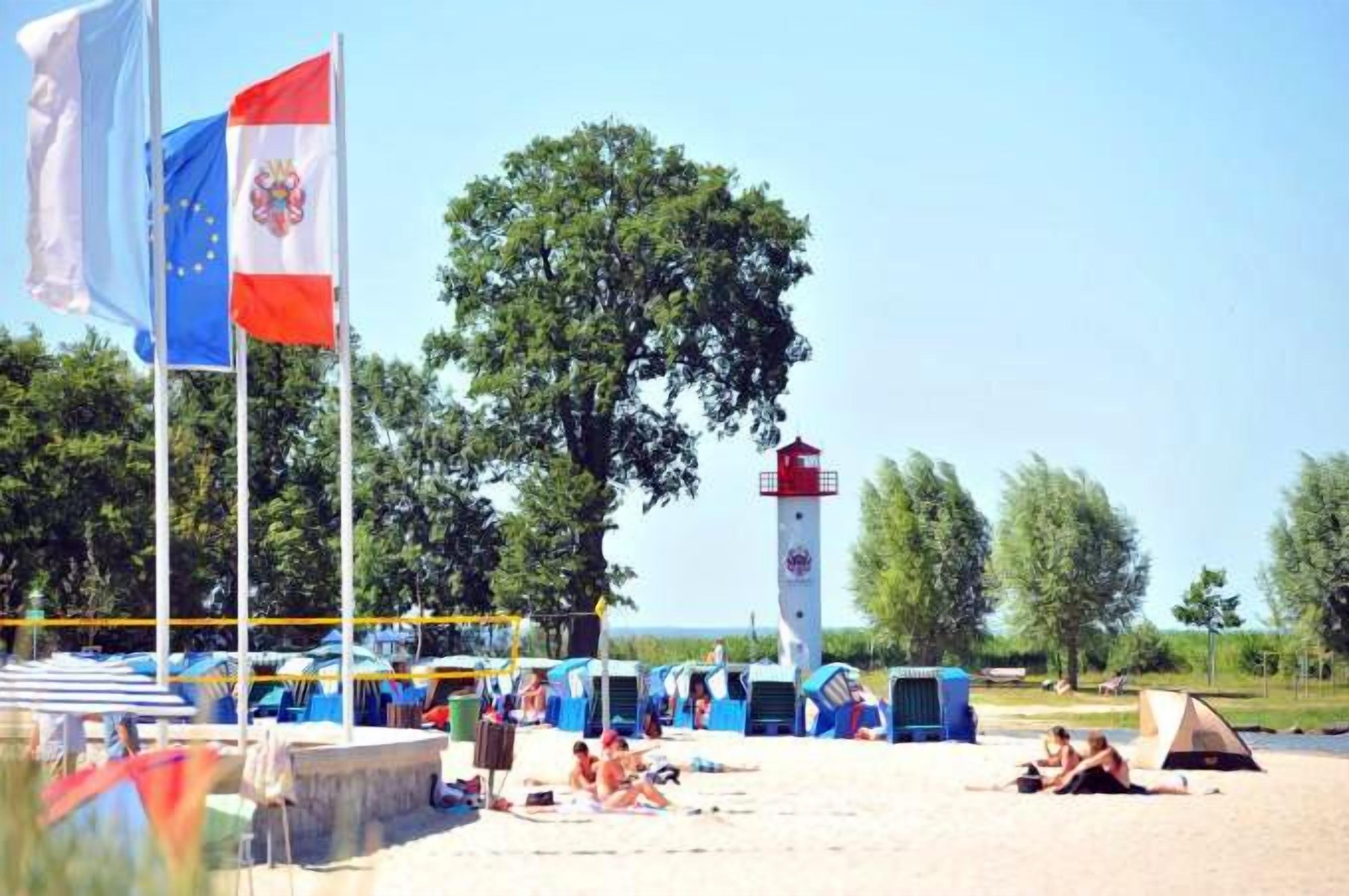 Une plage avec des drapeaux, un phare et des parasols.