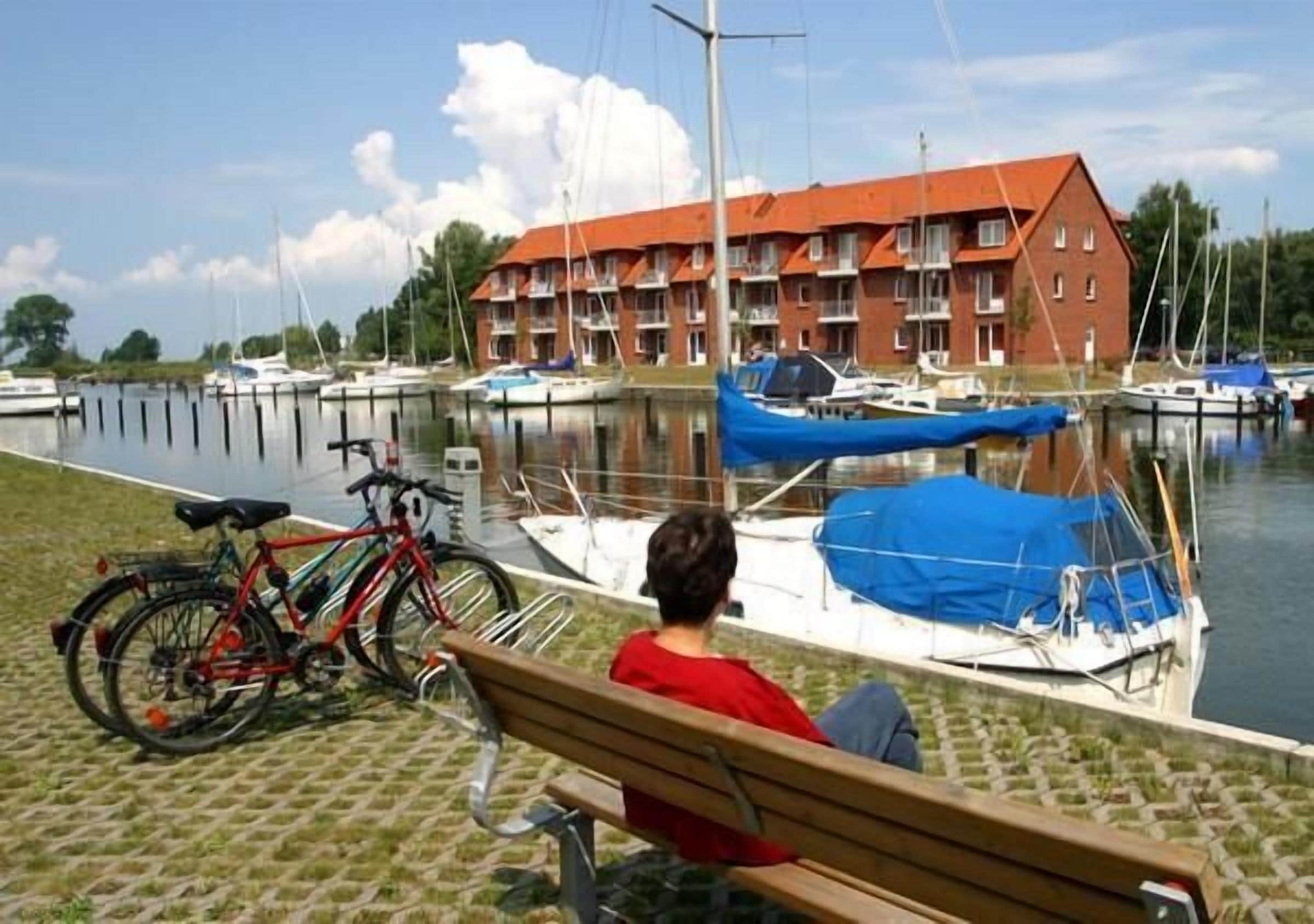 A person sitting on a bench overlooking a marina with boats and a building with a red roof.
