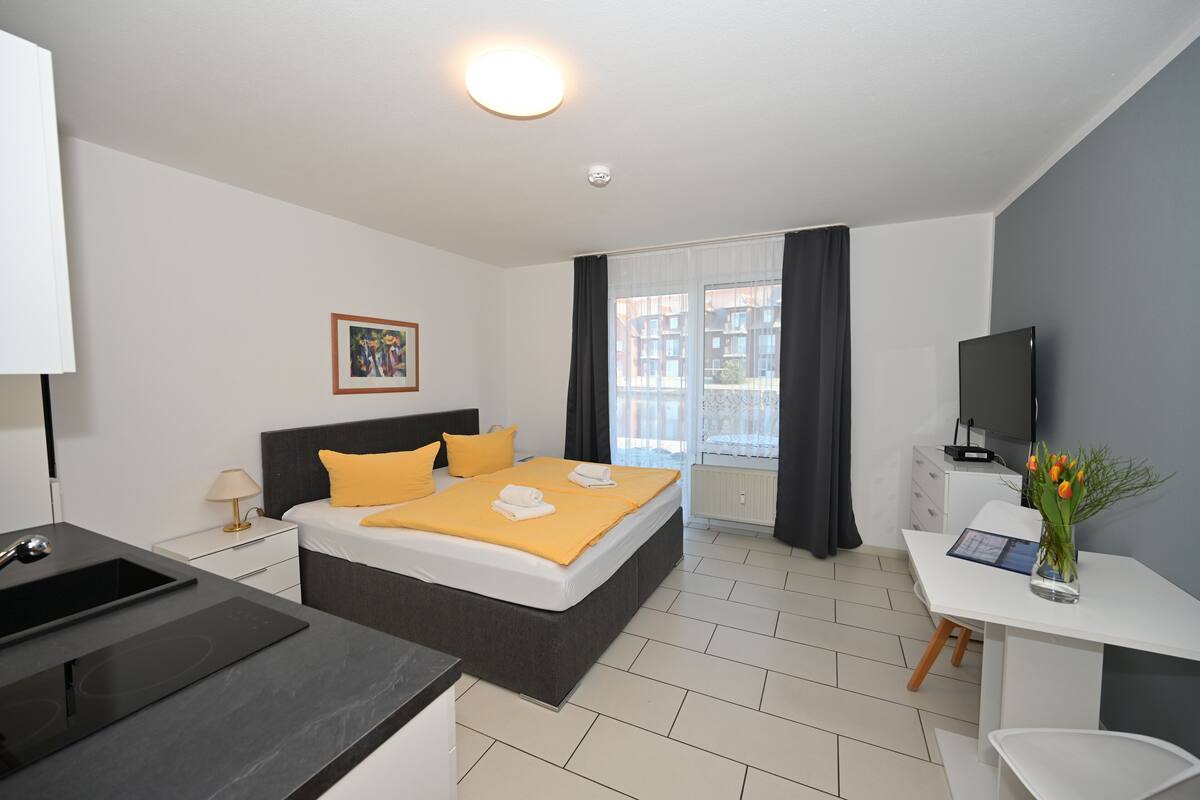 Ein modernes Hotelzimmer mit Bett, Nachttisch, Fernseher und Schreibtisch mit Stuhl.