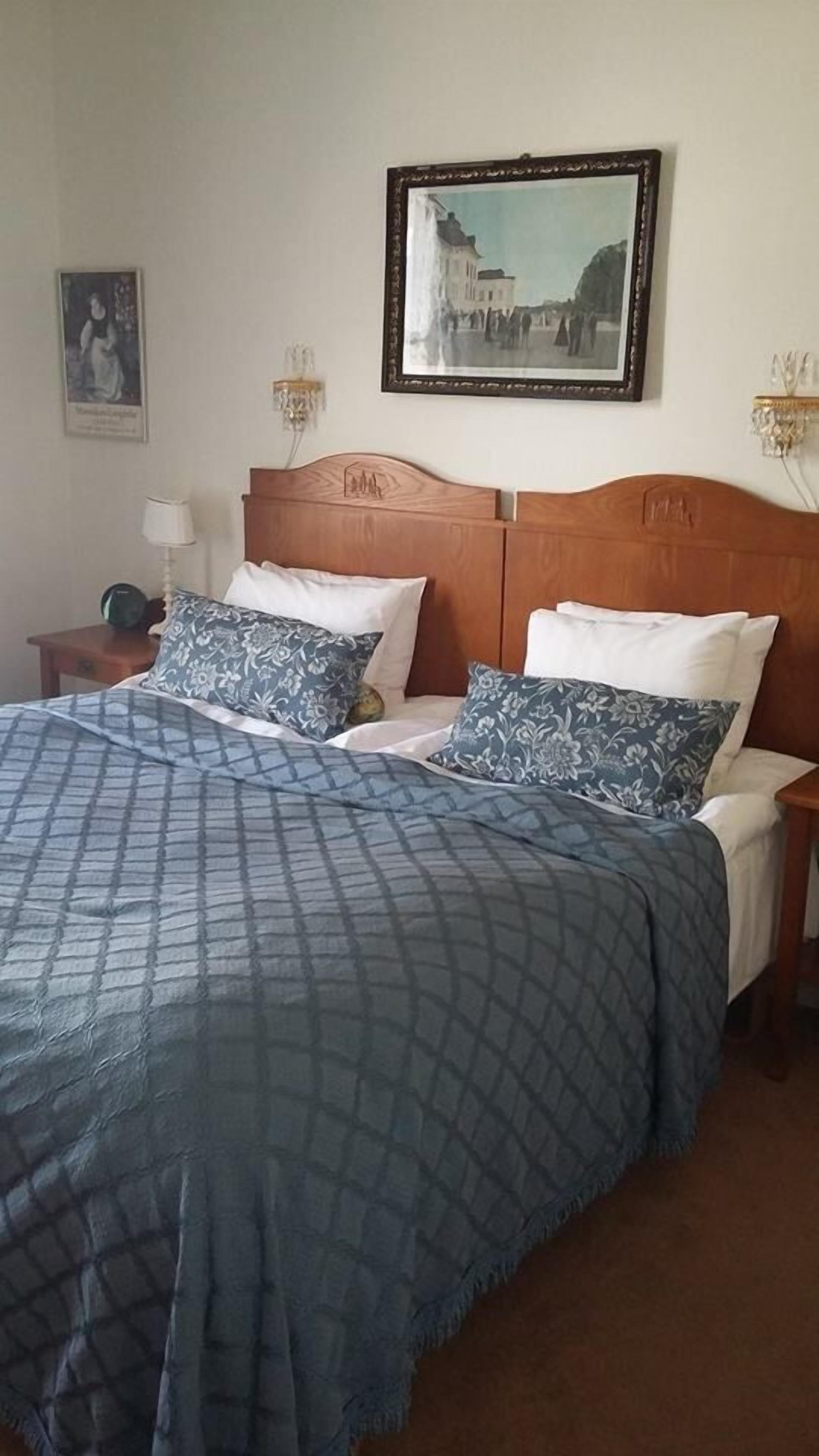 A bedroom with a large bed, two nightstands, a framed picture on the wall, and a lamp on the nightstand.