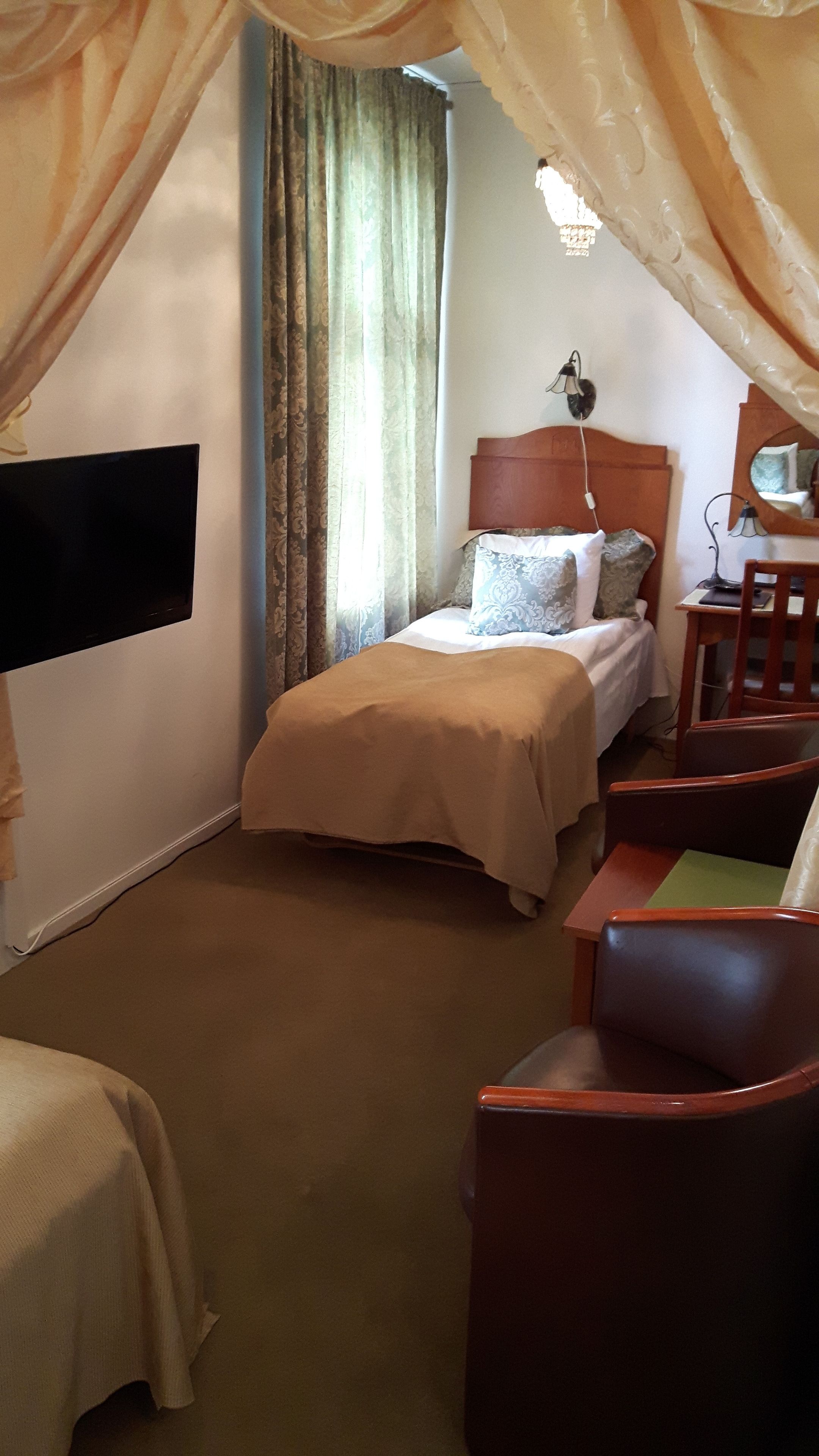 A hotel room with a bed, a desk, a chair, and a TV mounted on the wall.