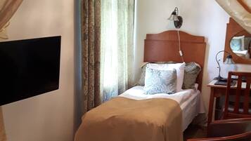 A hotel room with a bed, a desk, a chair, and a TV mounted on the wall.