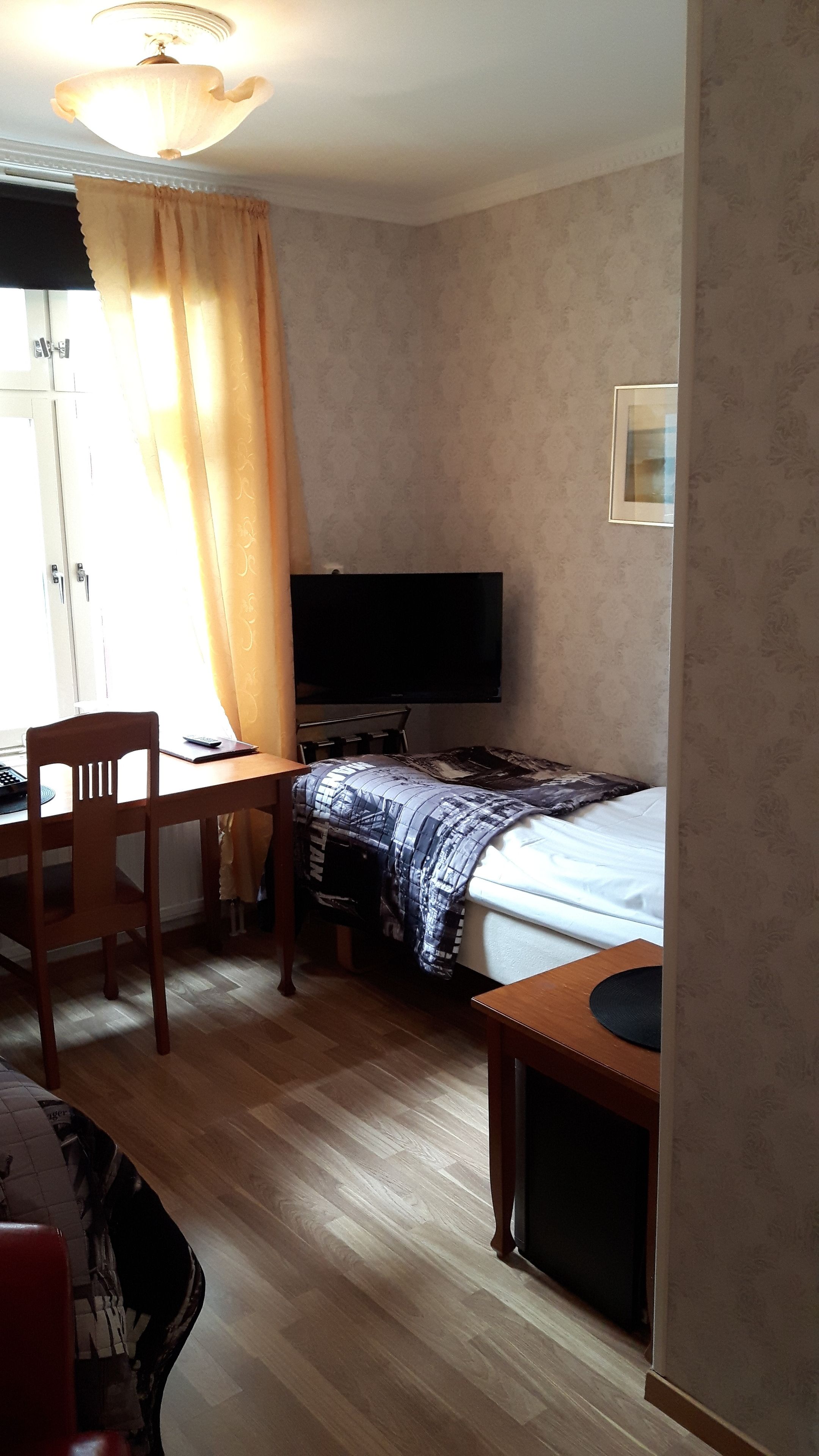 A hotel room with a bed, a desk with a chair, a television, and a window with curtains.