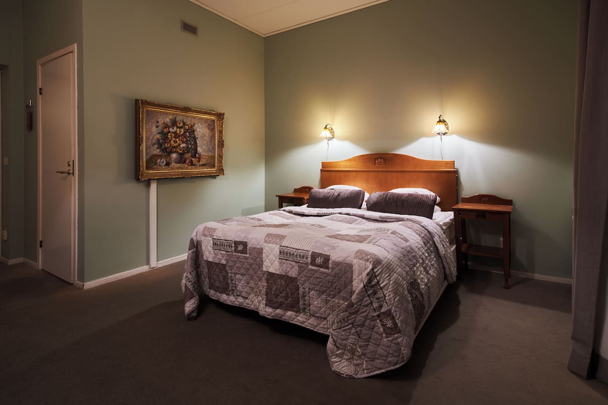 A bedroom with a large bed, two bedside tables with lamps, a door, and a framed picture on the wall.