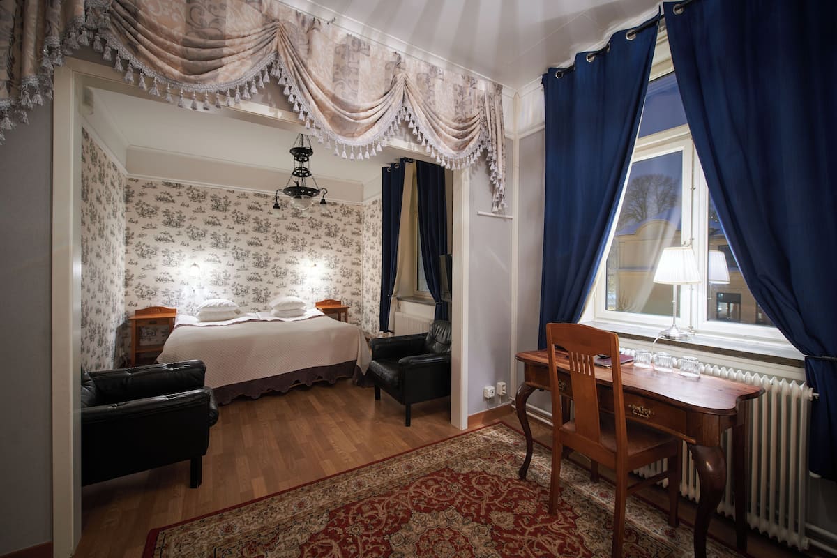 A bedroom with a bed, a desk, a chair, a radiator, and a window with curtains.