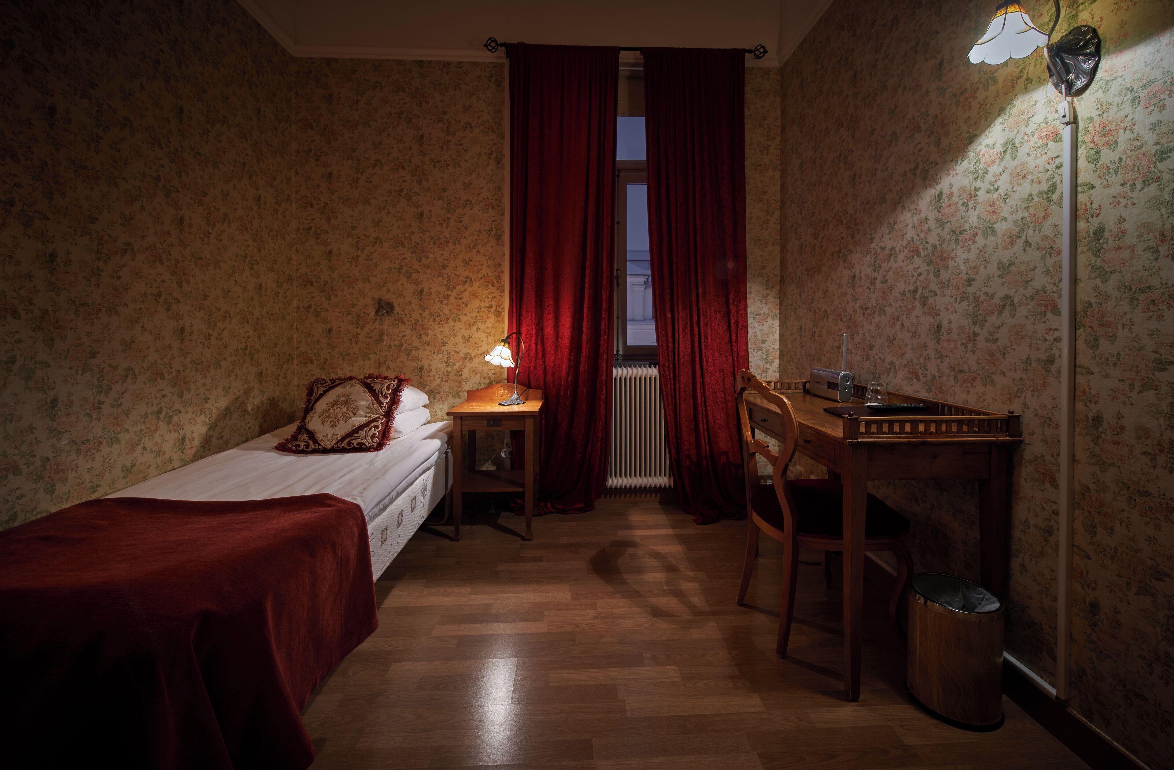 A small room with a single bed, a desk, a chair, and a radiator.
