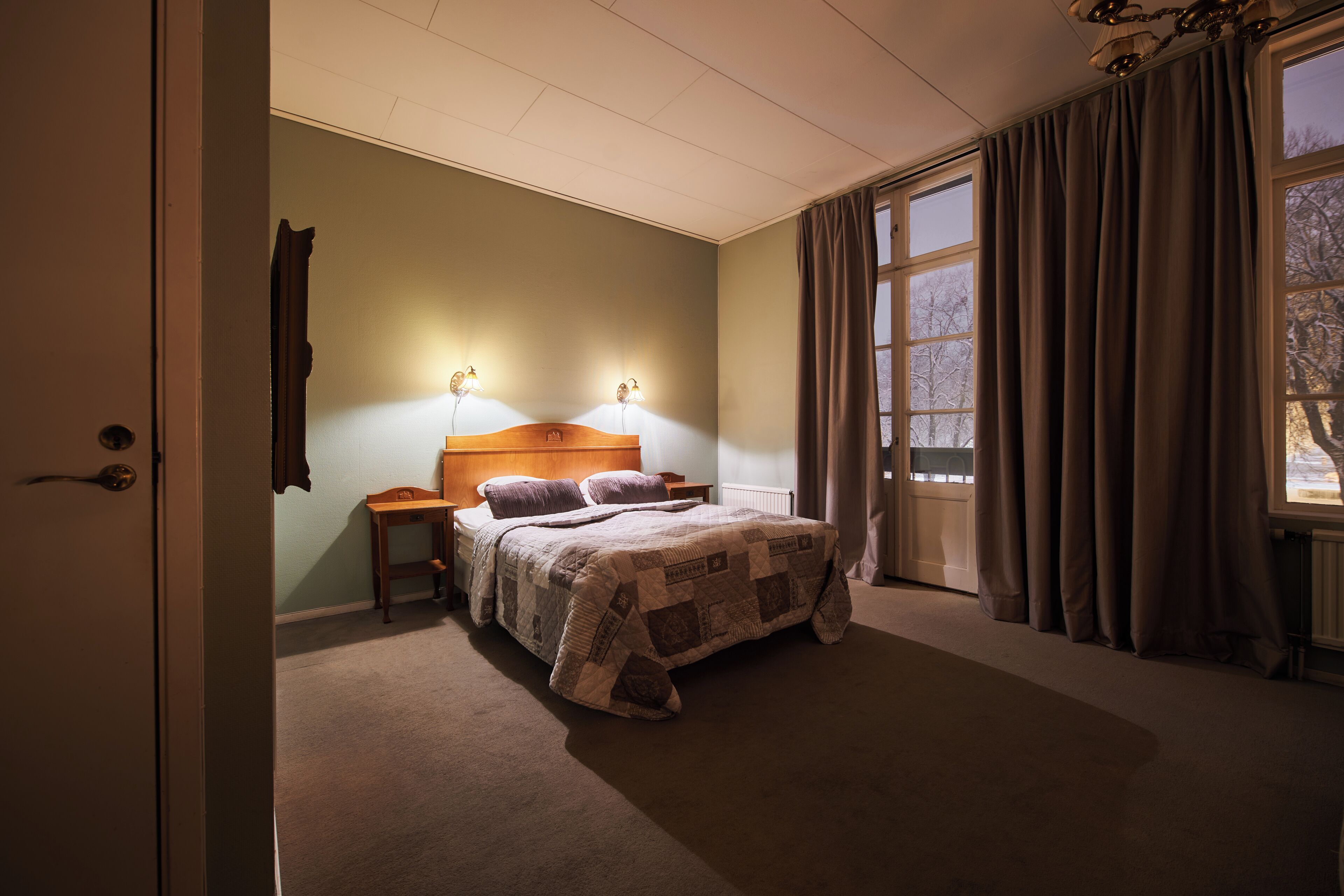 Une chambre à coucher avec un lit, des tables de chevet, une fenêtre avec des rideaux et une porte.