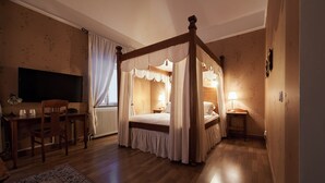 A four-poster canopy bed with a wooden frame and white bedding, a desk with a chair, a television, and a bedside table with a lamp. - Hotel Läckö (Lidköping)