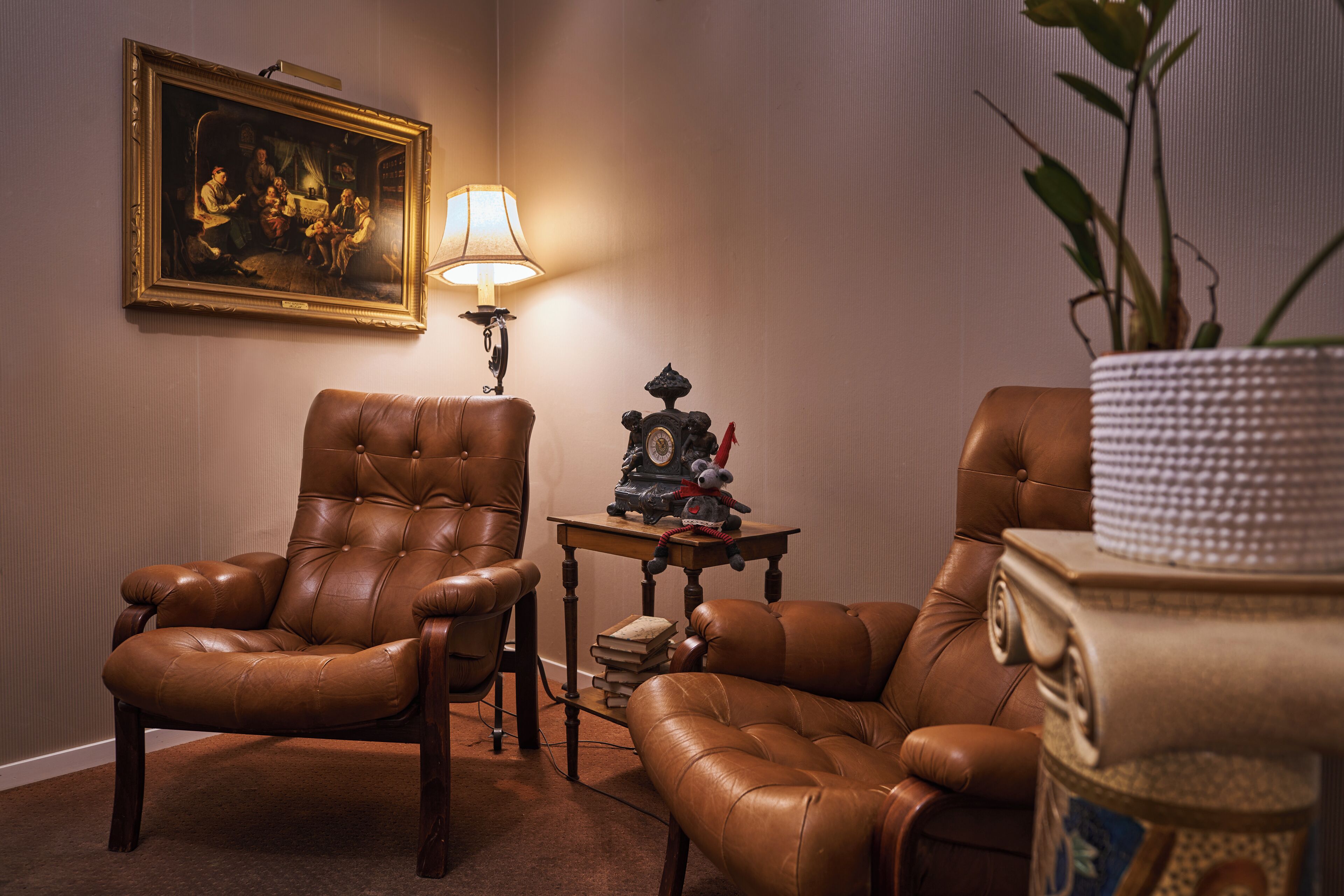 Una habitación con dos sillones de cuero marrón, una mesita con lámpara, un cuadro enmarcado y una planta en maceta.