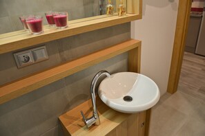 A modern bathroom with a white sink, a wooden vanity, and a shelf with two glasses of pink beverage.