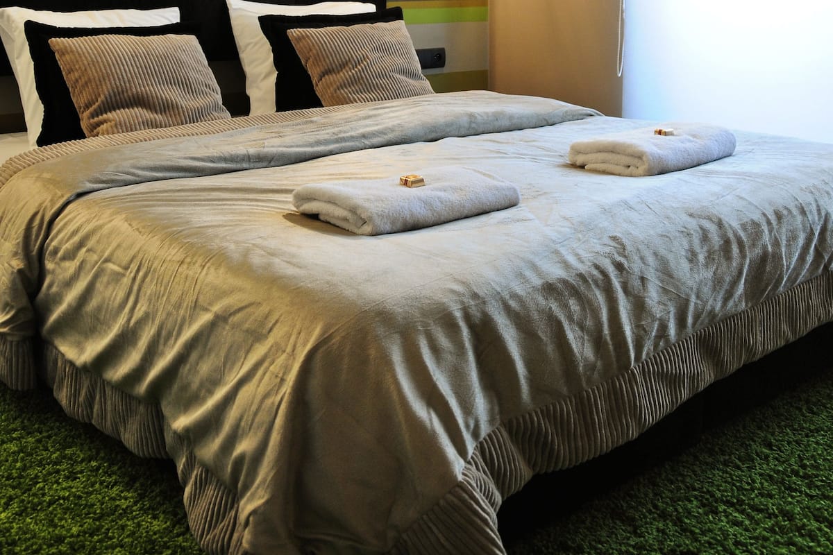 A double bed with a grey and white duvet, two pillows, and a green carpet.