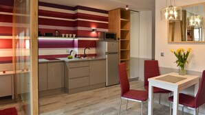 Une cuisine moderne avec des murs à rayures, un four à micro-ondes encastré et un réfrigérateur. On y trouve également un coin repas avec une table blanche et des chaises rouges.
