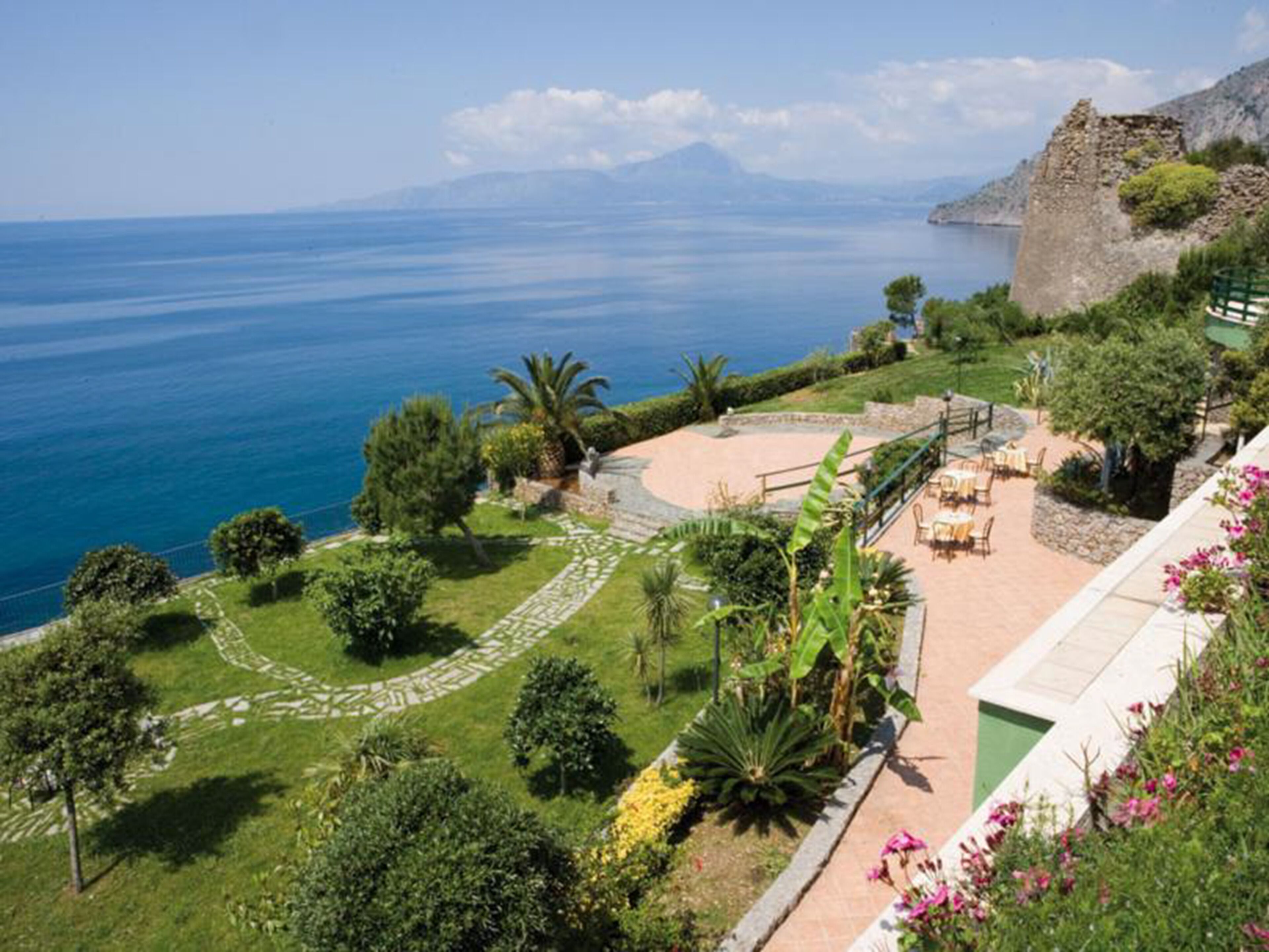 A coastal property with a patio area, lush greenery, and a view of the sea.
