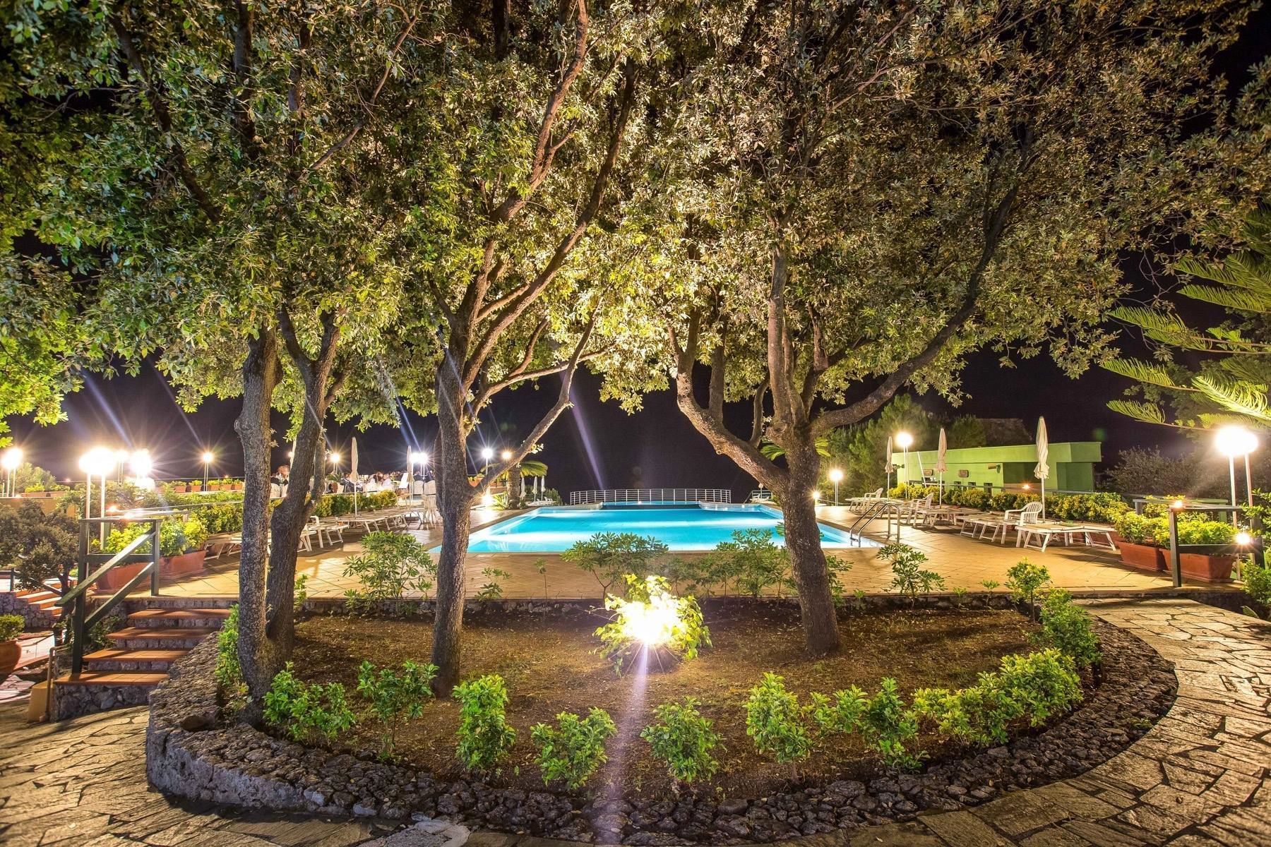 A nighttime swimming pool area with trees, lounge chairs, and a well-lit deck.