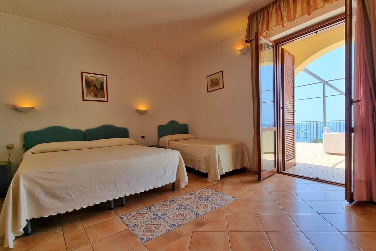 A hotel room with two beds, a balcony with a view, and a tiled floor.