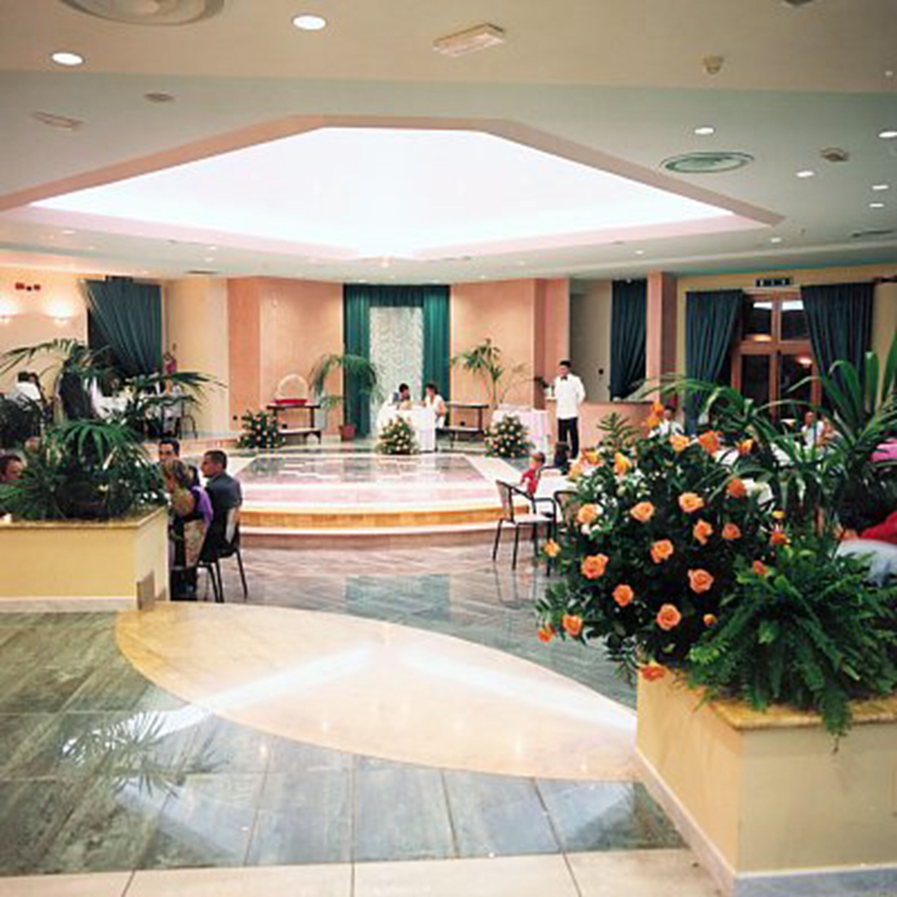 Un'ampia hall con un palco centrale, zone relax e piante in vaso.