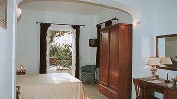 Un dormitorio con cama, un armario de madera, un escritorio con lámpara y una ventana con cortinas.