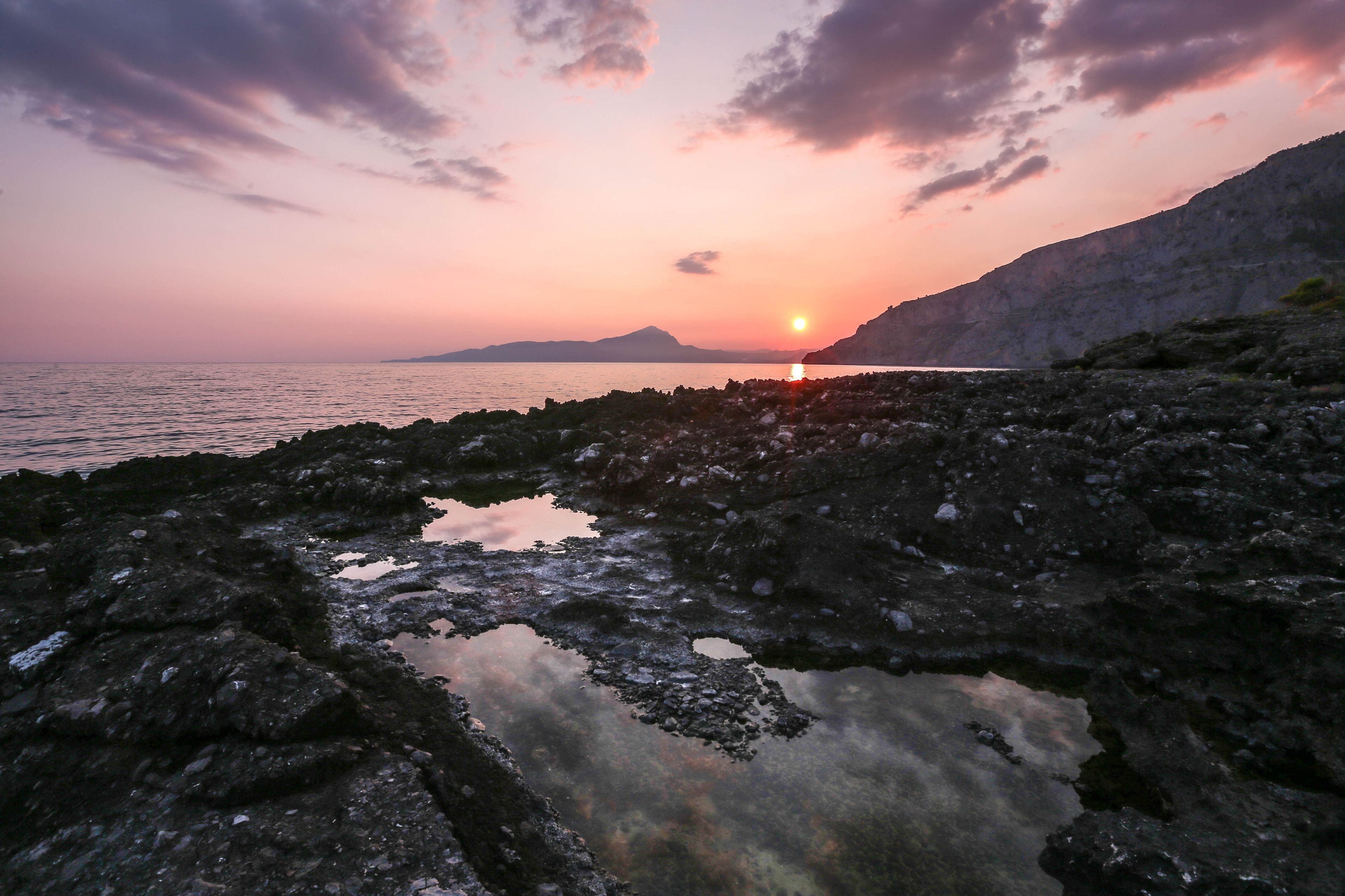 Eine felsige Küstenlinie mit Sonnenuntergang über dem Wasser.