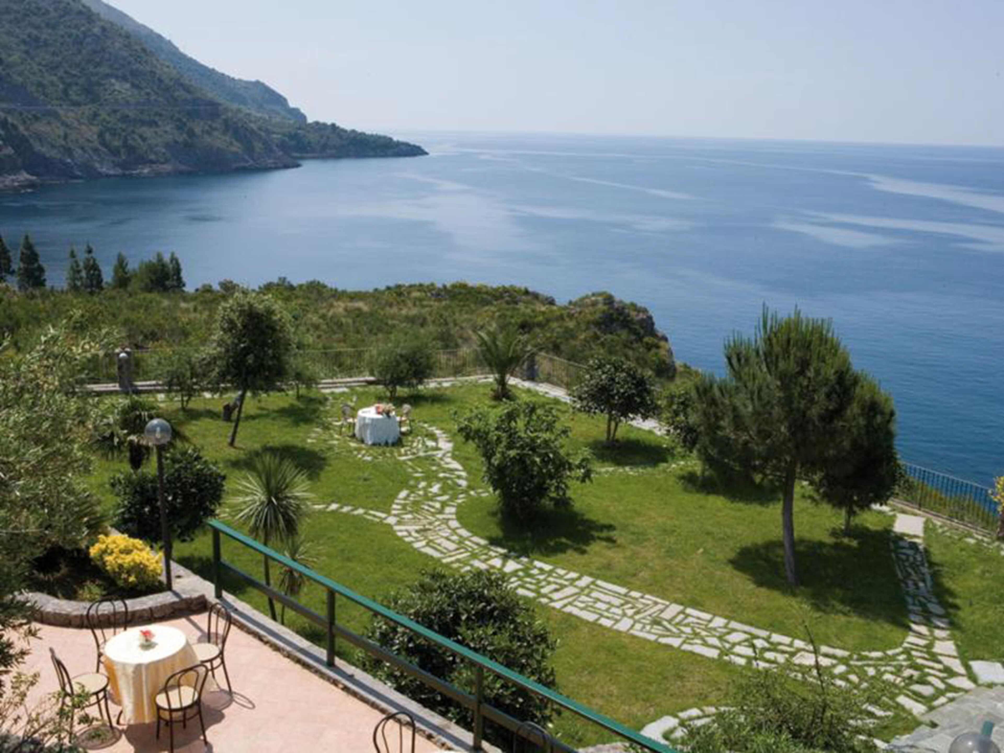 Terraço com vista para o mar, cercado por vegetação e um caminho de pedra.