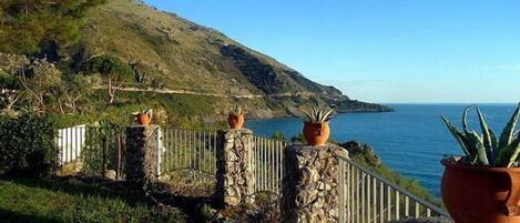 A coastal view with a stone fence, potted plants, and a clear sky.
