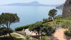 Eine Küstenansicht mit einem steinernen Pfad, der zu einem Gebäude führt, umgeben von Grün und mit Blick auf das ruhige Meer.