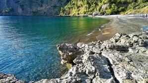 Eine felsige Küstenlinie mit klarem Wasser und einem Strand.