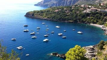 A coastal area with numerous boats anchored in clear blue waters, surrounded by rocky cliffs and dense greenery.