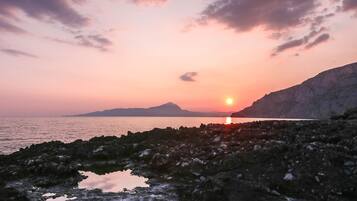 A sunset over a rocky coastline with a calm sea and distant mountains.