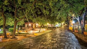 A stone-paved pathway leading to a gazebo under a canopy of trees, with ambient lighting and a small seating area.