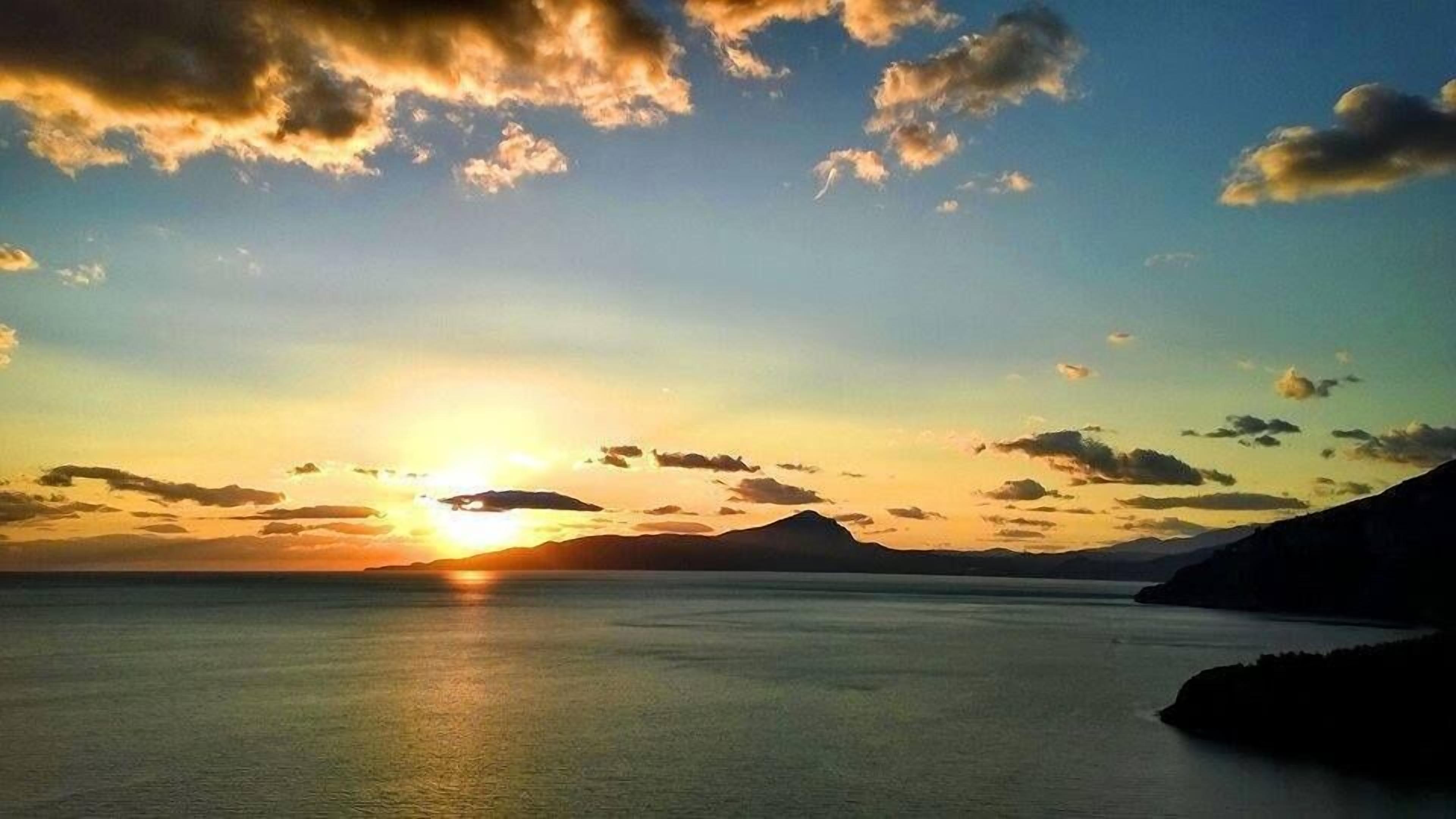 Un atardecer sobre una superficie de agua tranquila con montañas a lo lejos.