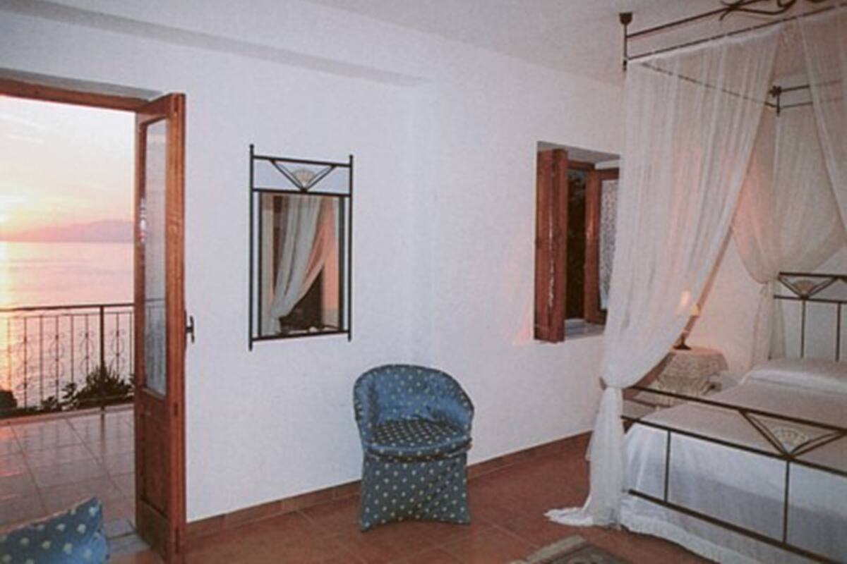 A bedroom with a bed, a chair, a mirror, and a view of the sunset.