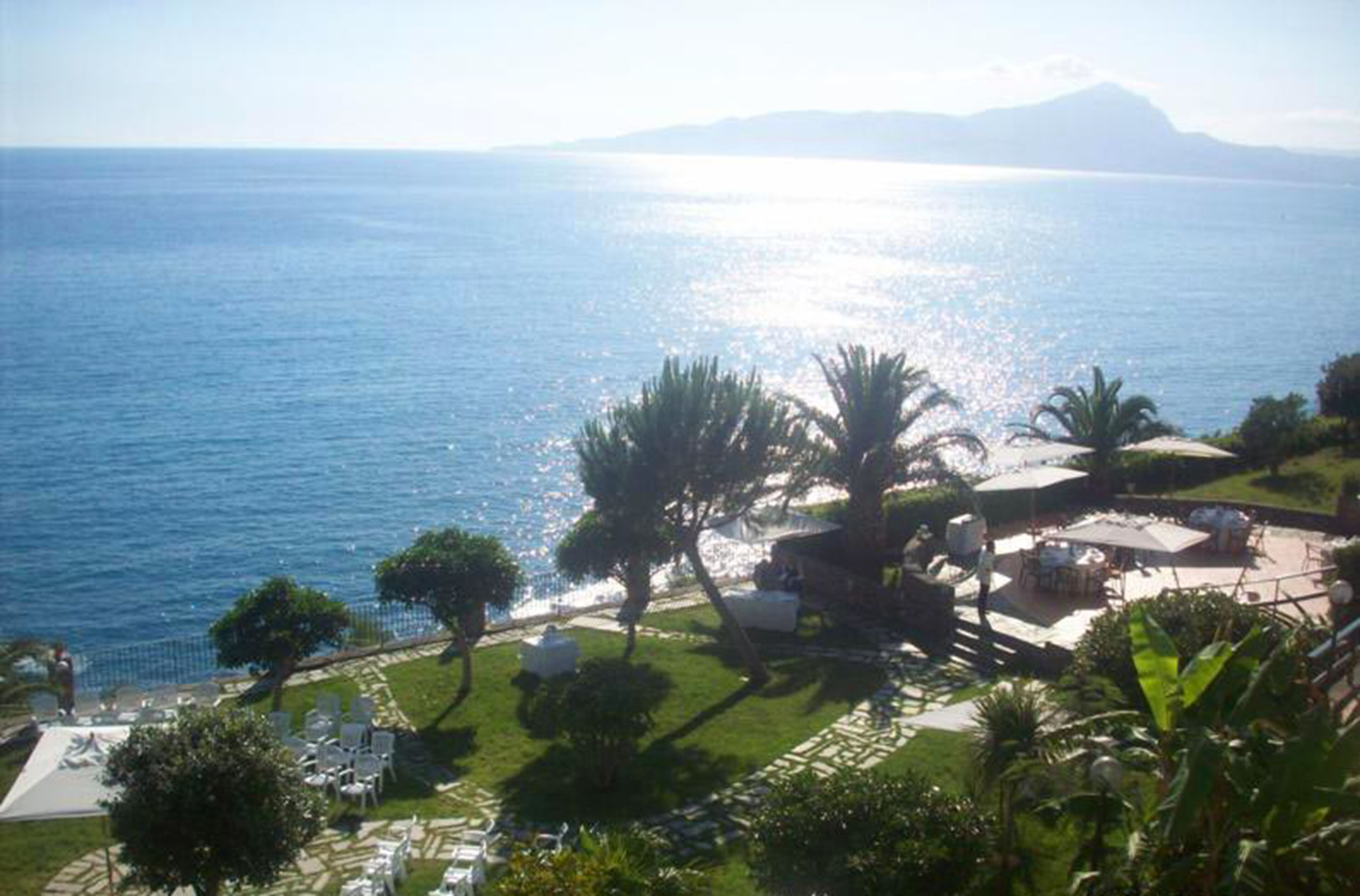 A coastal view with a clear sky, a beach area with lounge chairs, and a mountainous backdrop.