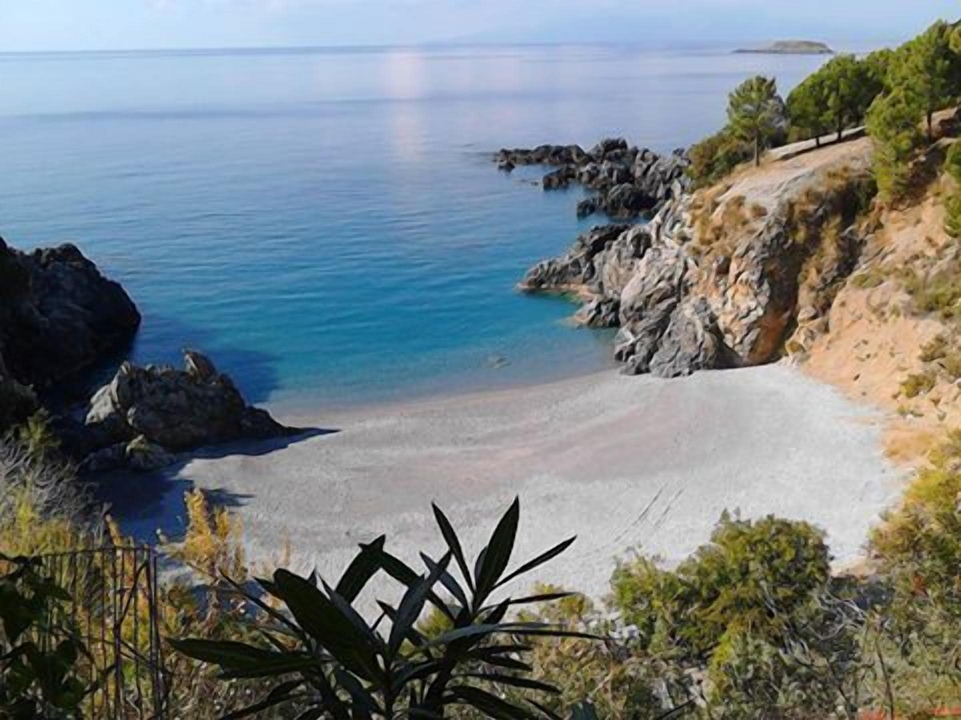 A coastal landscape with a sandy beach, rocky outcrops, and sparse vegetation.