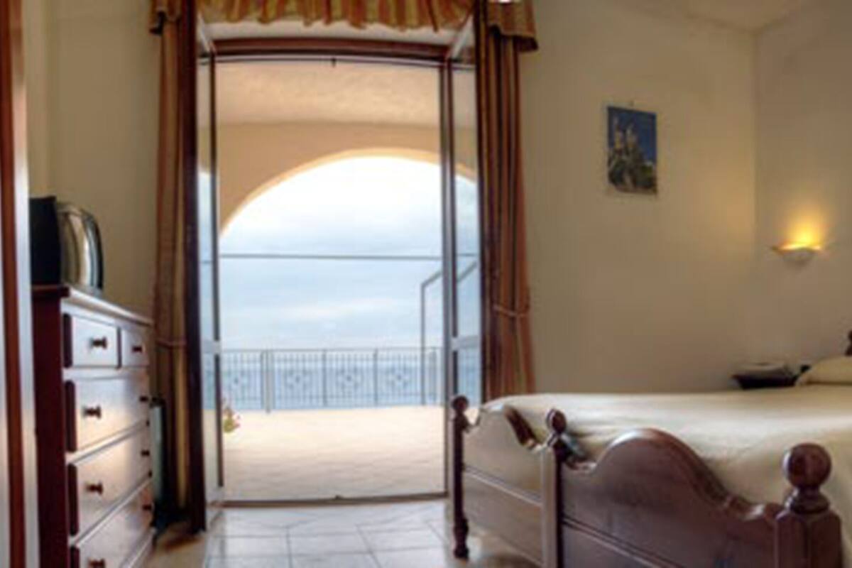 A bedroom with a bed, a nightstand, a dresser, and a view of a balcony.