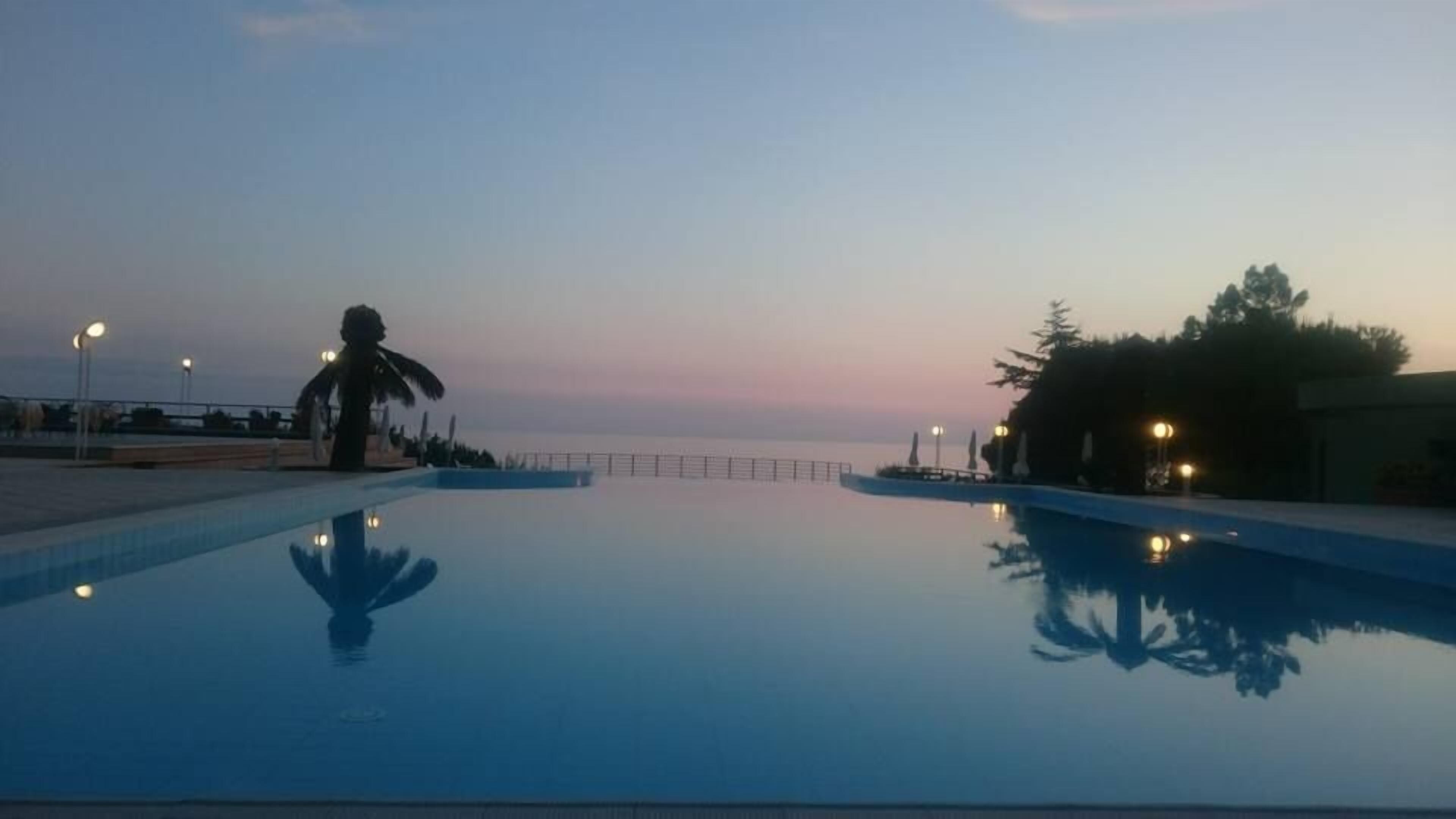 Une piscine offrant une vue dégagée sur la mer et un coucher de soleil en toile de fond.