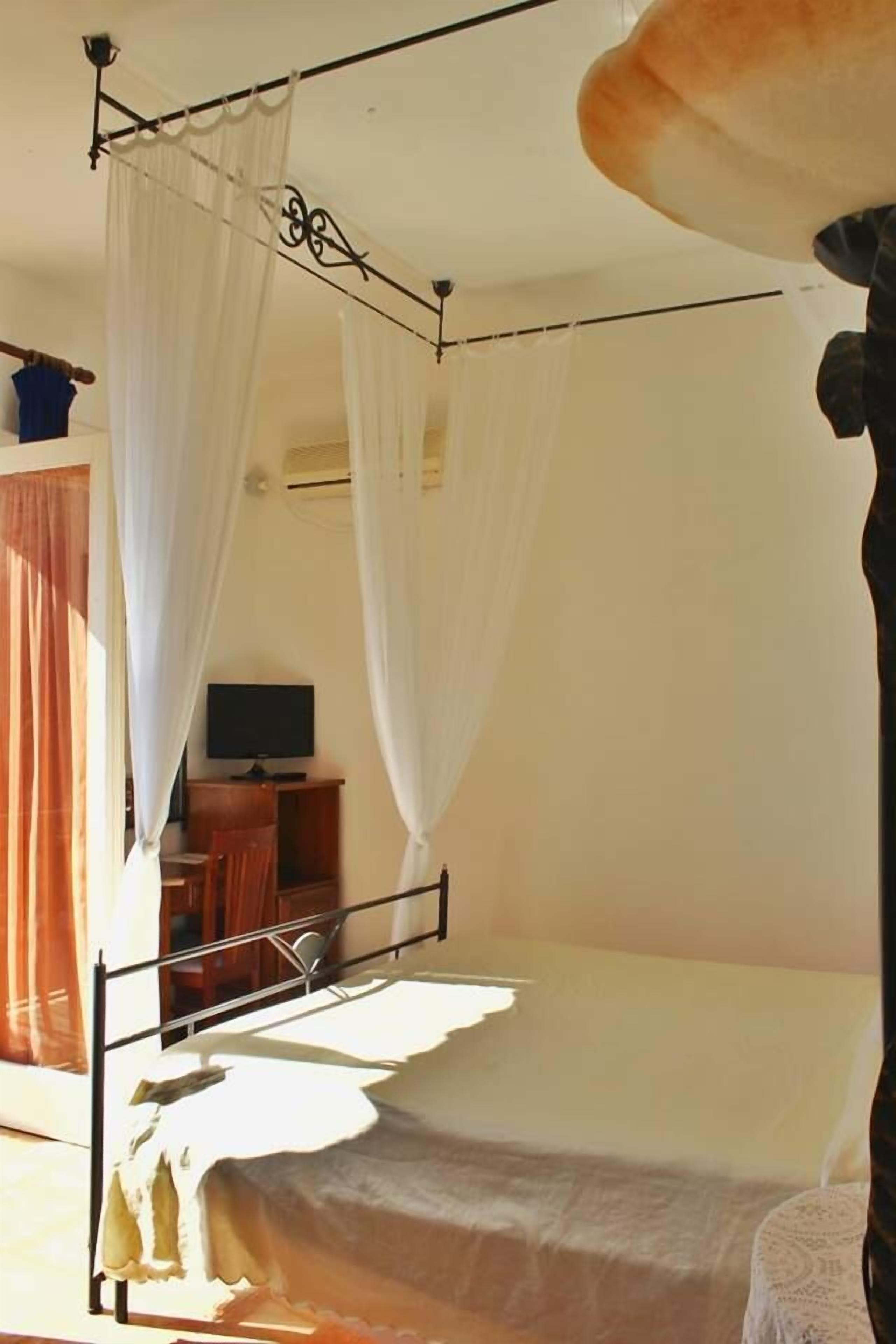 A single bed with a canopy, a television on a wooden stand, and a window with curtains.
