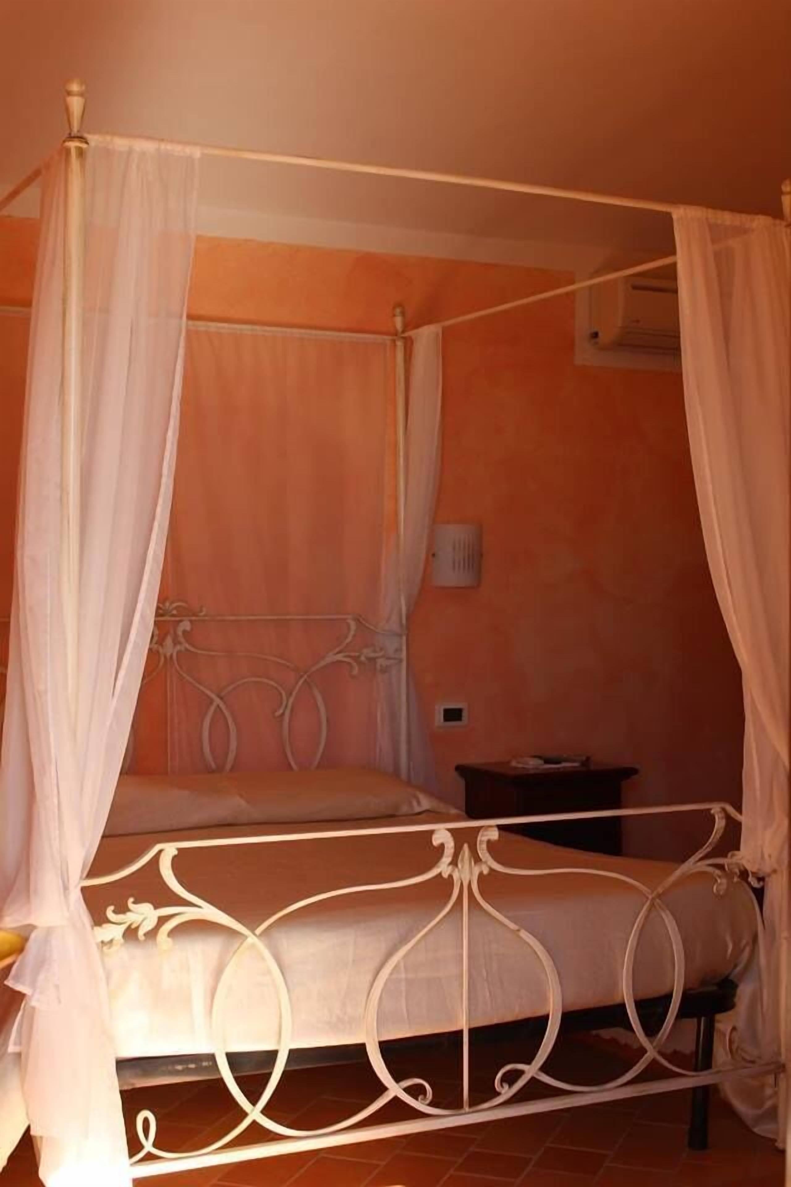 A four-poster canopy bed with a white metal frame and a white bedspread.