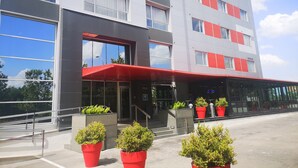 A modern building with a red awning, large windows, and potted plants in front.