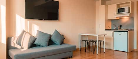 A modern living room with a grey sofa, a flat-screen TV, and a compact kitchen area with a microwave.